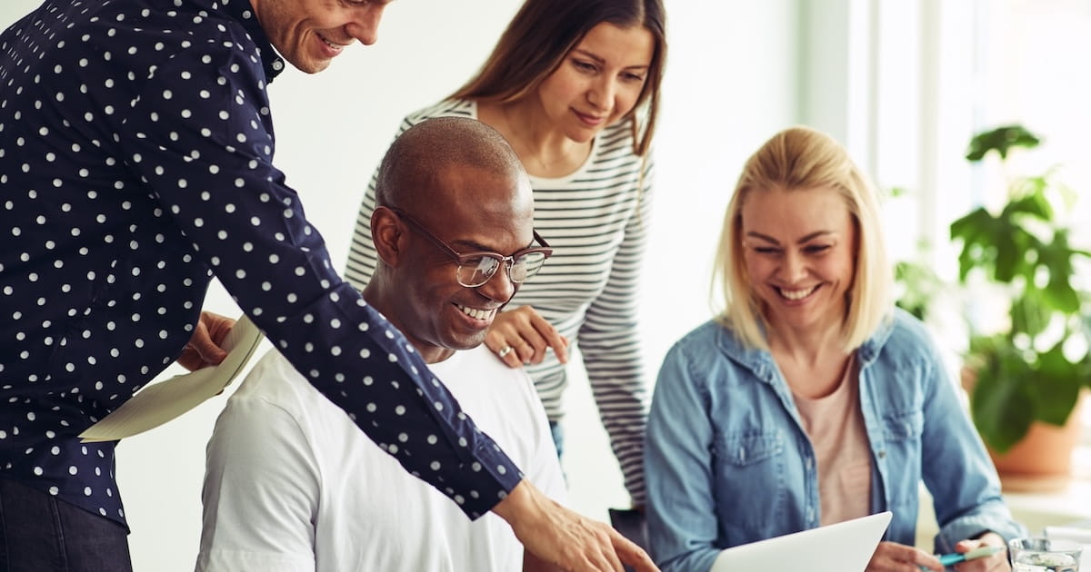 Marketing team collaborating around a laptop in a bright office